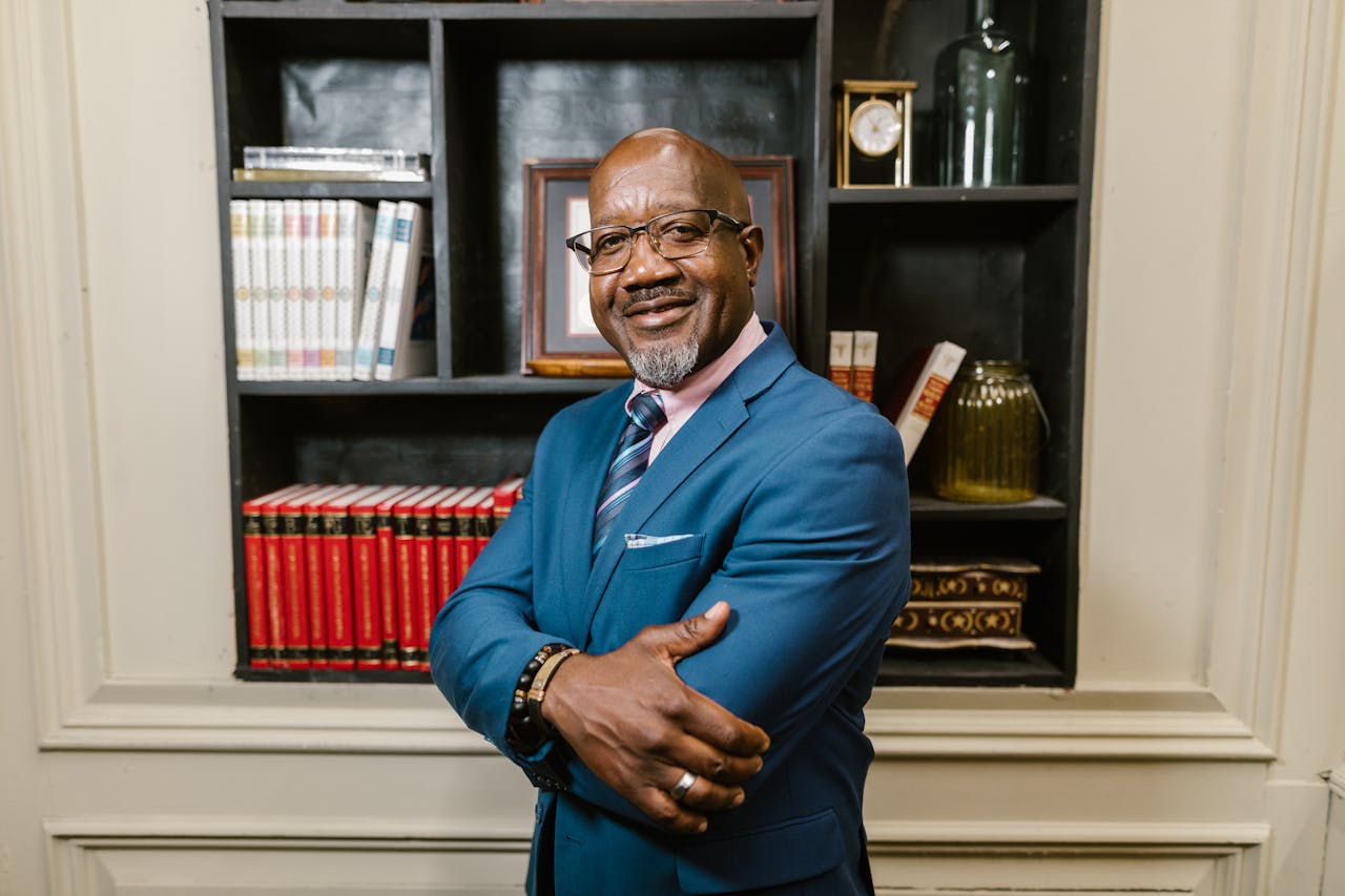 Mature businessman with glasses smiling confidently in an elegant office with a bookshelf background.